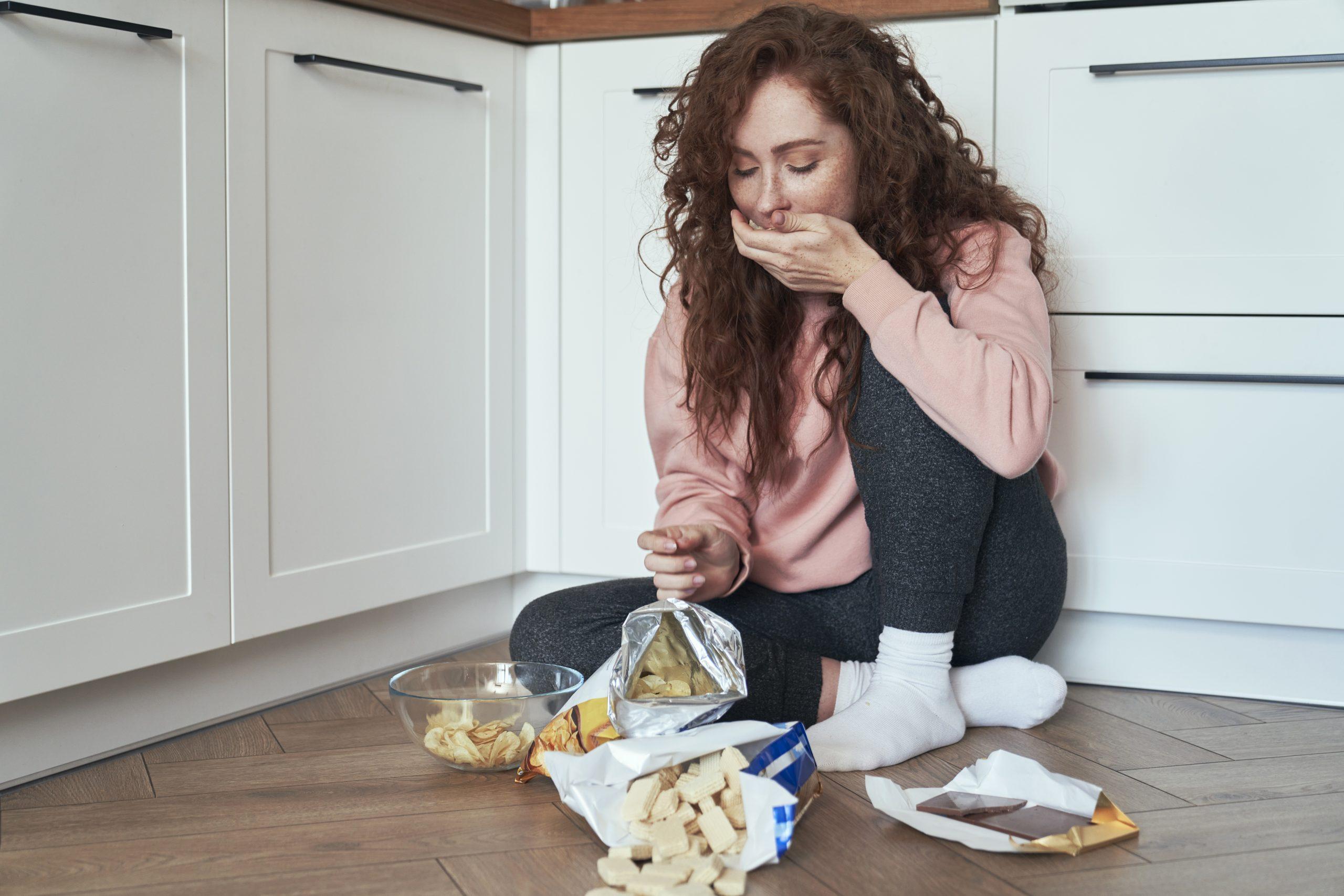 Young caucasian woman having eating disorder and eating greedily on the floor